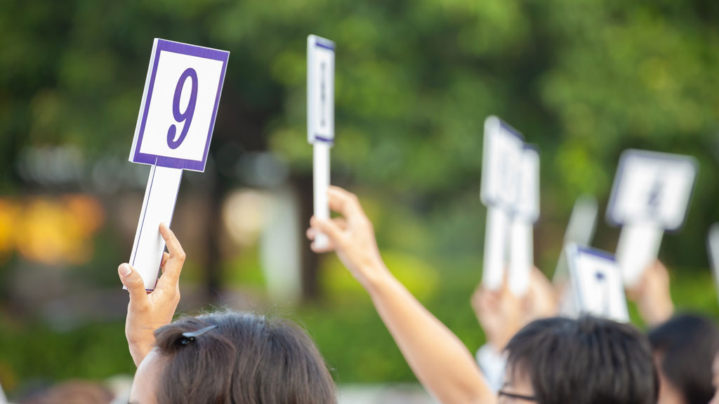 Illustrative photo of a group of people at an auction, holding up bidding signs