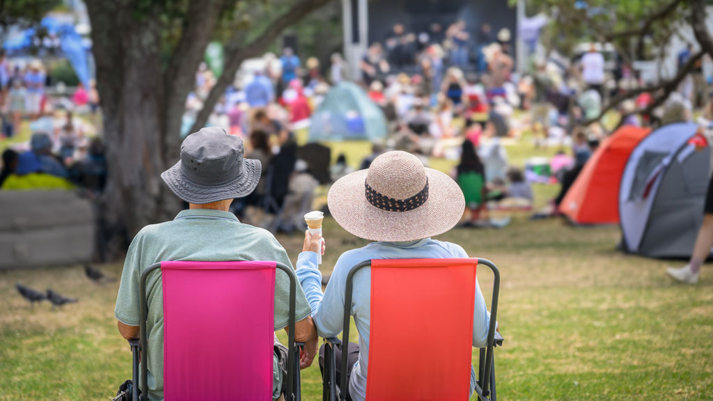 Illustrative photo of a couple sitting on lawn chairs while attending an outdoor concert in a park